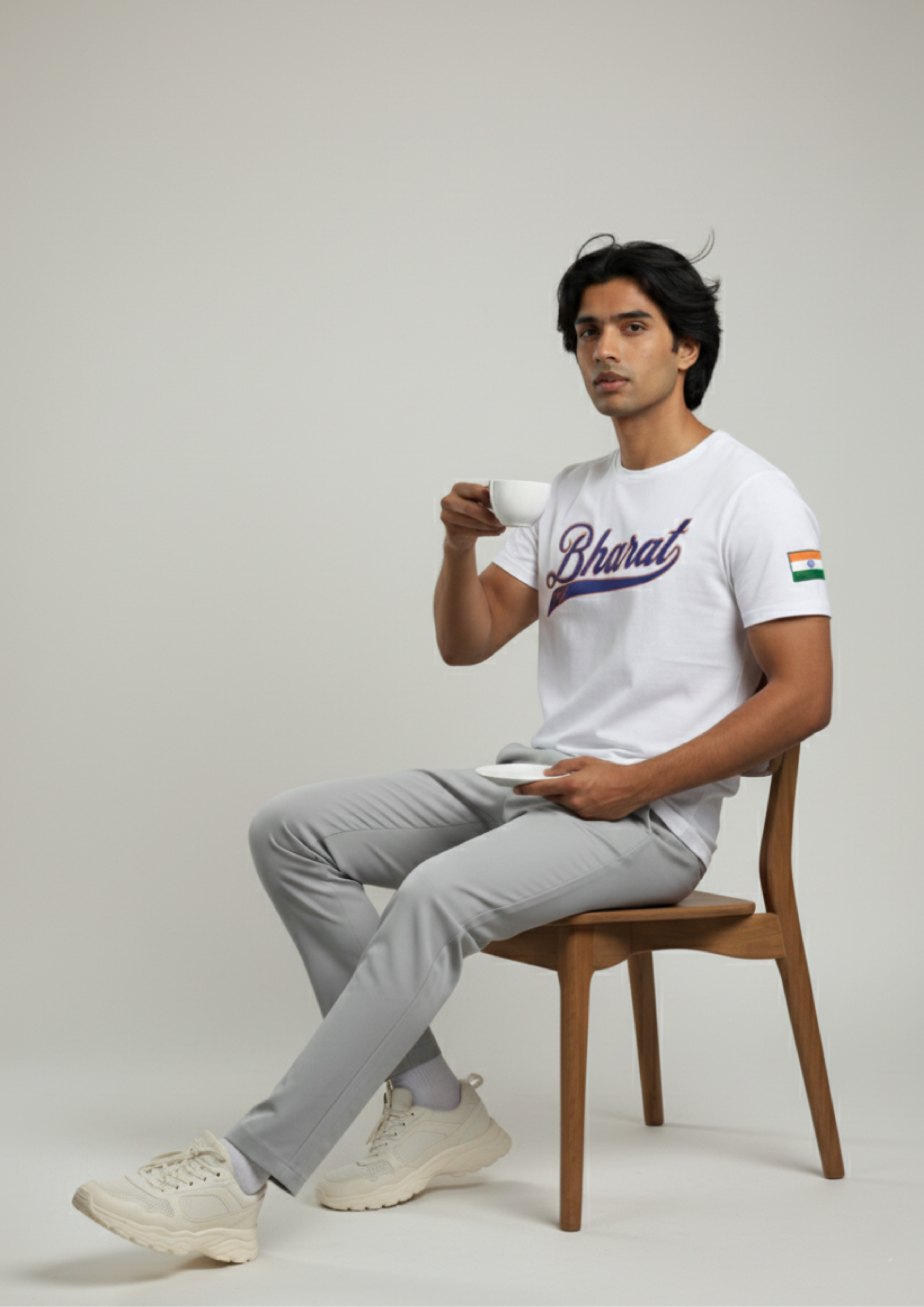 Man sitting on a chair holding a cup, wearing a white t-shirt with text and graphics.